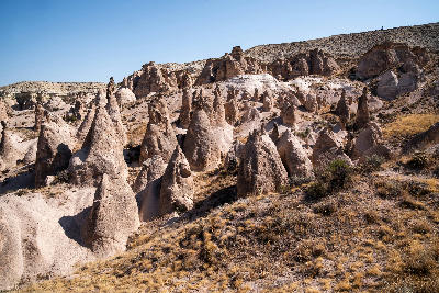 Panoramic view of the cone-shaped volcanic rock formations and eroded landscape of Devrent Valley (Imagination Valley) in Cappadocia, Turkey, under a clear summer sky.