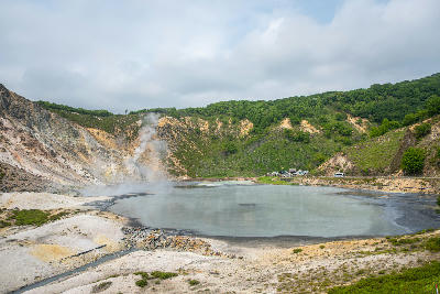 Wide view of Oyunuma Pond with steaming geothermal vents and mineral shoreline in Noboribetsu, Hokkaido, Japan.