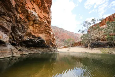 Waterhole beneath rugged red rock walls and river gums in Ormiston Gorge.