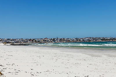 Wide white-sand beach at Yzerfontein with turquoise Atlantic waters and the coastal town visible along the shoreline in the background.