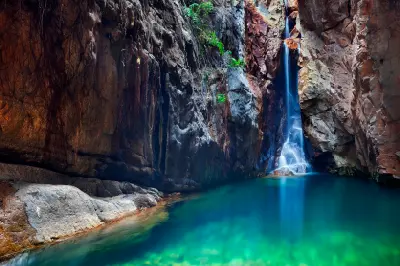 Waterfall cascades between steep rock walls into a clear turquoise plunge pool in El Questro Gorge.
