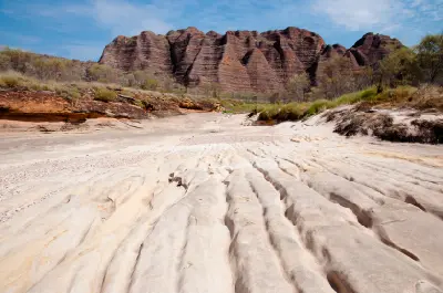 Pale eroded channels in the dry bed of Piccaninny Creek lead toward the striped sandstone formations of the Bungle Bungle Range.