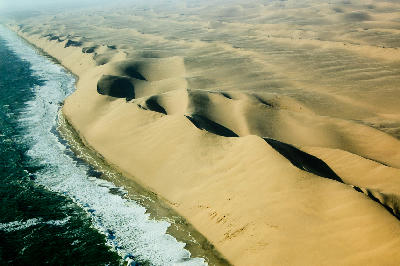 Aerial landscape of massive Namib Desert dunes meeting the Atlantic Ocean along the Skeleton Coast in Namibia.