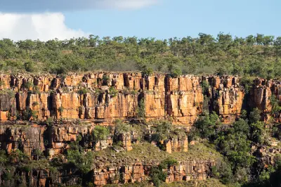 Towering orange-red sandstone cliffs rise above scattered native vegetation in Chamberlain Gorge.