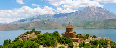 Holy Cross Church surrounded by trees on Akdamar Island, with Lake Van and rugged mountains in the background.