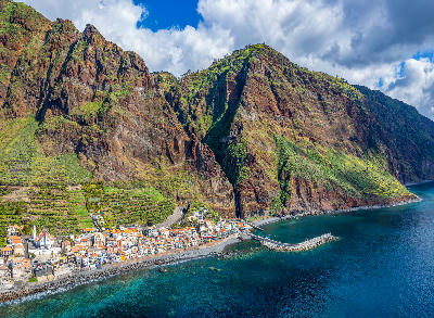 Paul do Mar village along Madeira’s southwest coast, with compact coastal buildings set beneath towering volcanic cliffs and the Atlantic Ocean.