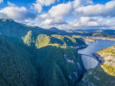 Aerial view of Gordon Dam and its reservoir amid forested mountains in southwest Tasmania.