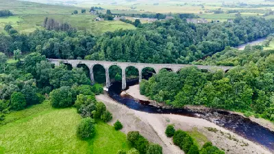Aerial view of Lambley Viaduct crossing the River South Tyne, showing its long row of stone arches, winding river and densely wooded valley near Haltwhistle, Northumberland.