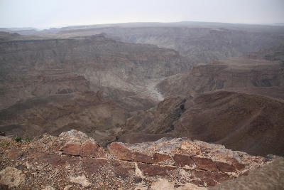 Wide hazy view from the rim of Fish River Canyon showing layered cliffs and the winding canyon floor in southern Namibia.