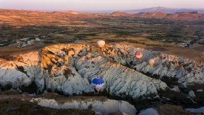 Hot air balloons flying over the white volcanic rock formations of White Valley at sunrise in Cappadocia, Turkey.