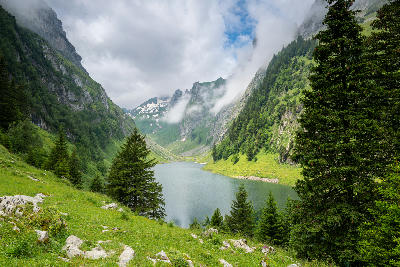 Fälensee in a narrow alpine valley below Saxer Lücke, surrounded by steep limestone slopes, forested sides, and low cloud in the Alpstein mountains, Switzerland.
