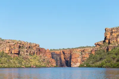 Calm blue water of the King George River beneath towering red sandstone cliffs and rugged Kimberley escarpments.