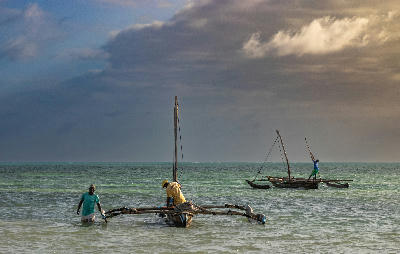 Fishermen with a traditional wooden outrigger dhow in the shallow waters off Jambiani Beach, Zanzibar, Tanzania.