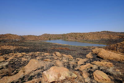 Small dam surrounded by rocky hills and burned grassland in Suikerbosrand Nature Reserve, Gauteng.