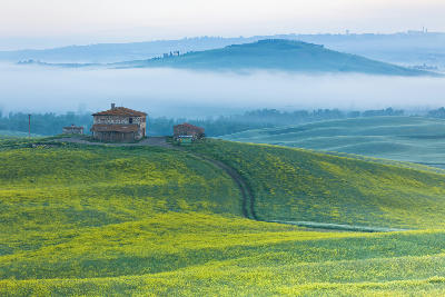 Farmhouse at Podere Terrapille surrounded by misty hills at sunrise in Val d’Orcia, Tuscany, Italy.