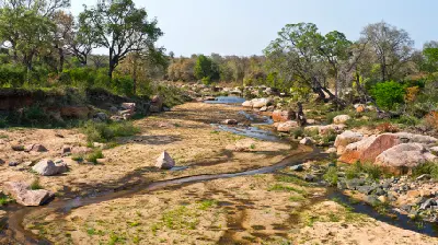 Rocky section of the Sabie River with sandy banks, scattered granite boulders and riverine woodland in Kruger National Park.