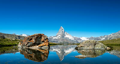 Matterhorn reflected in Stellisee with foreground rocks on a clear summer day, Switzerland.