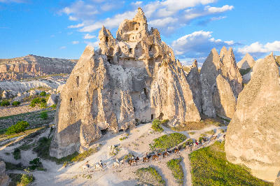 Horse riders passing rock-cut cave dwellings and volcanic formations in Rose Valley, Cappadocia, Turkey.