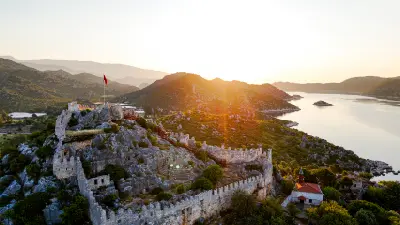 Aerial sunset view of Simena Castle and Kaleköy overlooking the islands and Mediterranean waters of Kekova, Türkiye.