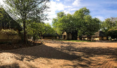 Thatched accommodation buildings and mature trees in the central area of Lower Sabie Rest Camp.