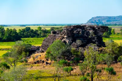Layered sandstone rock formation overlooking green floodplains and distant escarpments in Kakadu National Park, Northern Territory, Australia.