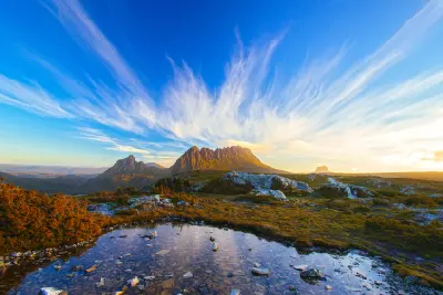Cradle Mountain illuminated by warm evening light above alpine tarns and rocky moorland in Tasmania, Australia.