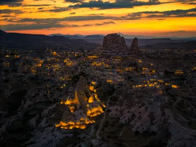 Uçhisar Castle and illuminated fairy chimneys at sunset above Uçhisar village in Cappadocia, Turkey.