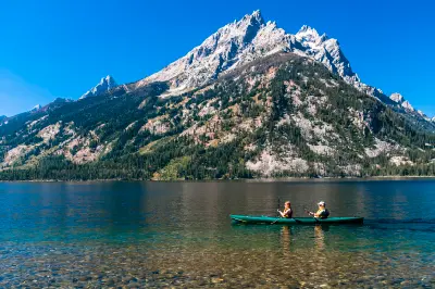Kayakers on Jenny Lake with rocky shoreline and the Teton Range rising behind, Grand Teton National Park, Wyoming, USA.