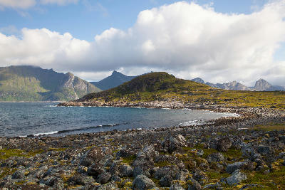 Rocky shoreline at Mefjordvær with Knuten peak and surrounding mountains across the fjord on Senja island, Norway