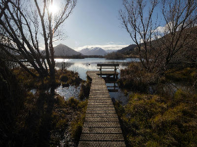 Wooden boardwalk leading through wetlands to Glenorchy Lagoon with mountains in the distance near Lake Wakatipu, South Island, New Zealand.