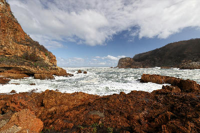 Rocky shoreline and crashing waves below the Knysna Heads, where rugged sandstone cliffs frame the dramatic entrance to the Knysna Estuary on South Africa's Garden Route.