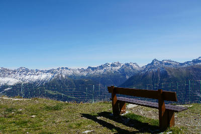Bench at Bettmerhorn viewpoint overlooking the Swiss Alps with distant peaks and glacier views.
