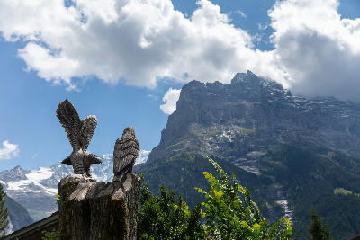 Wooden eagle sculptures in the foreground with rocky alpine peaks rising behind near Grindelwald First, Bernese Alps, Switzerland.