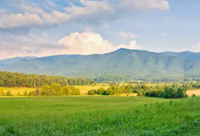 Green fields and forested mountain ridges in Cades Cove beneath soft evening clouds in the Great Smoky Mountains.