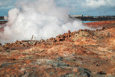 Steam rising from fumaroles at Gunnuhver geothermal field on the Reykjanes Peninsula, Iceland, with red and orange mineral deposits in the foreground.