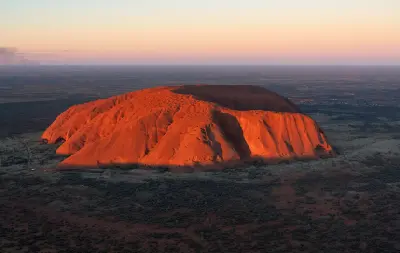 Uluru rises from the vast desert landscape of Central Australia in warm evening light.