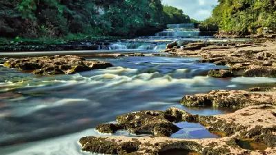 Long-exposure view of the Lower Falls at Aysgarth Falls, showing the River Ure flowing over stepped limestone ledges surrounded by woodland in the Yorkshire Dales.