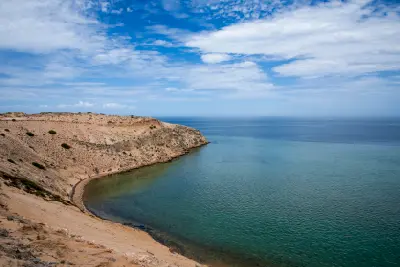 Curved ochre cliffs descend into clear turquoise water beneath a wide blue sky at Eagle Bluff.