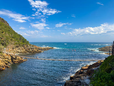 Suspension bridge crossing Storms River Mouth between rocky cliffs and the Indian Ocean in Tsitsikamma National Park, South Africa.