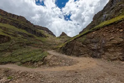 Sharp gravel hairpin bend on Sani Pass surrounded by steep rocky cliffs and alpine slopes in the Drakensberg Mountains between South Africa and Lesotho.