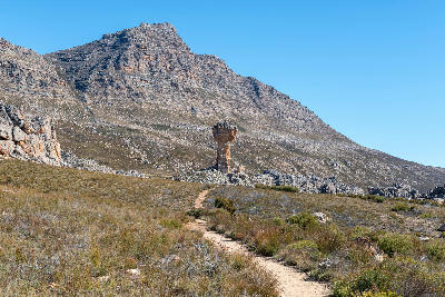 Hiking trail leading towards the Maltese Cross rock formation in the Cederberg Mountains, surrounded by rugged sandstone slopes and mountain scenery beneath a clear blue sky.