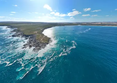 Aerial view of Point Ellen at Vivonne Bay, showing a rocky headland, breaking Southern Ocean waves, turquoise bay waters and distant sandy shoreline.