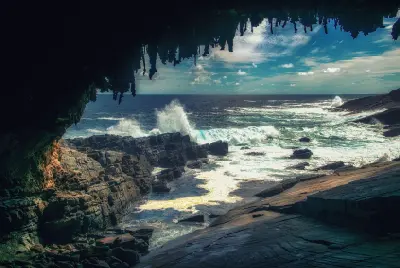 Ocean waves breaking against dark coastal rocks beneath Admirals Arch, with hanging limestone formations framing the view on Kangaroo Island.