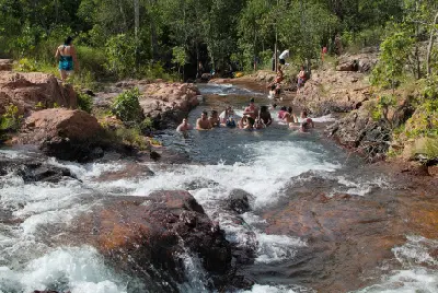 Visitors swimming and relaxing in natural rock pools surrounded by sandstone ledges and flowing cascades at Buley Rockhole, Litchfield National Park, Australia.