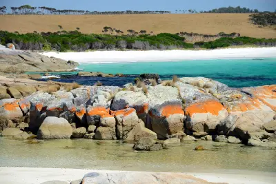 Orange lichen-covered granite rocks beside turquoise water and white sand at The Gardens, Bay of Fires, Tasmania.