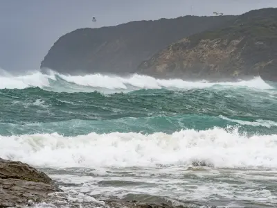 Large waves breaking below the rugged Cape Otway headland with the lighthouse visible in the distance, Victoria.