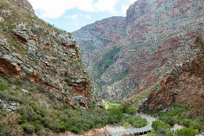 Curving mountain road passing through steep red sandstone canyon walls in Meiringspoort in the Western Cape of South Africa.