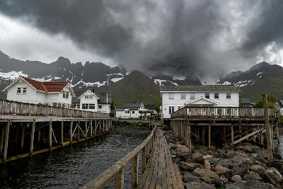Mefjordvær village on Senja with wooden pier, coastal houses, and snow patches on mountains under low clouds in northern Norway