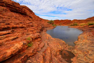 Rock pool surrounded by layered red sandstone in Watarrka National Park near Kings Canyon, Northern Territory, Australia.