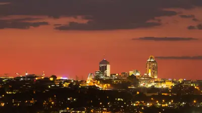 Evening view of the Sandton skyline in Johannesburg, with illuminated office towers against an orange sunset sky.